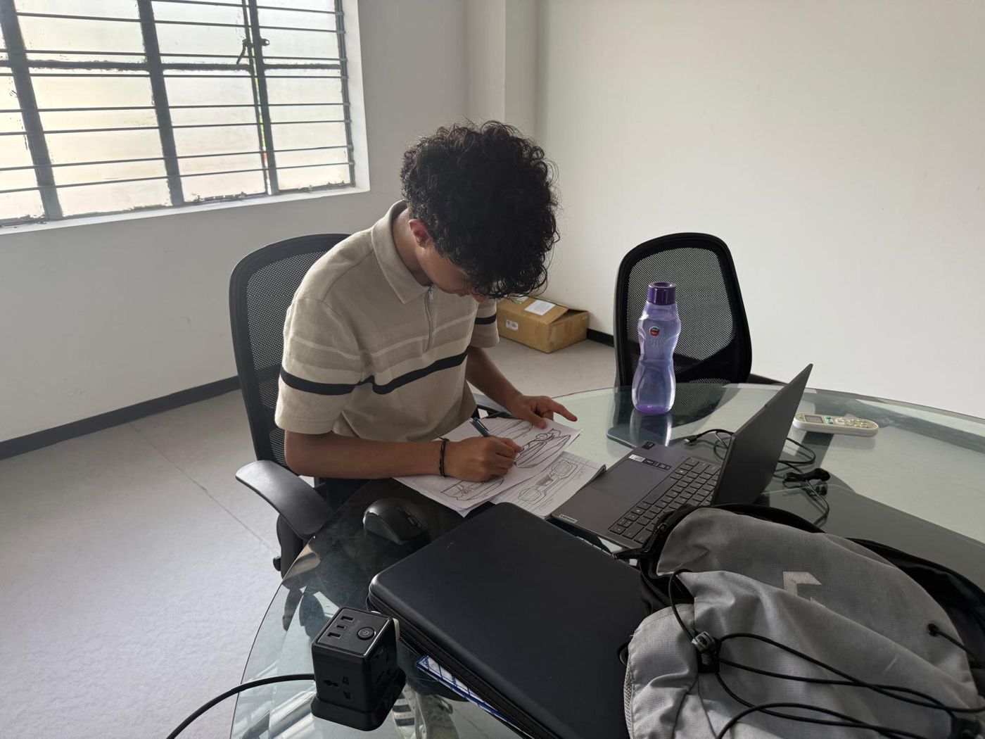 Kanishk at a desk sketching car designs on paper next to a laptop